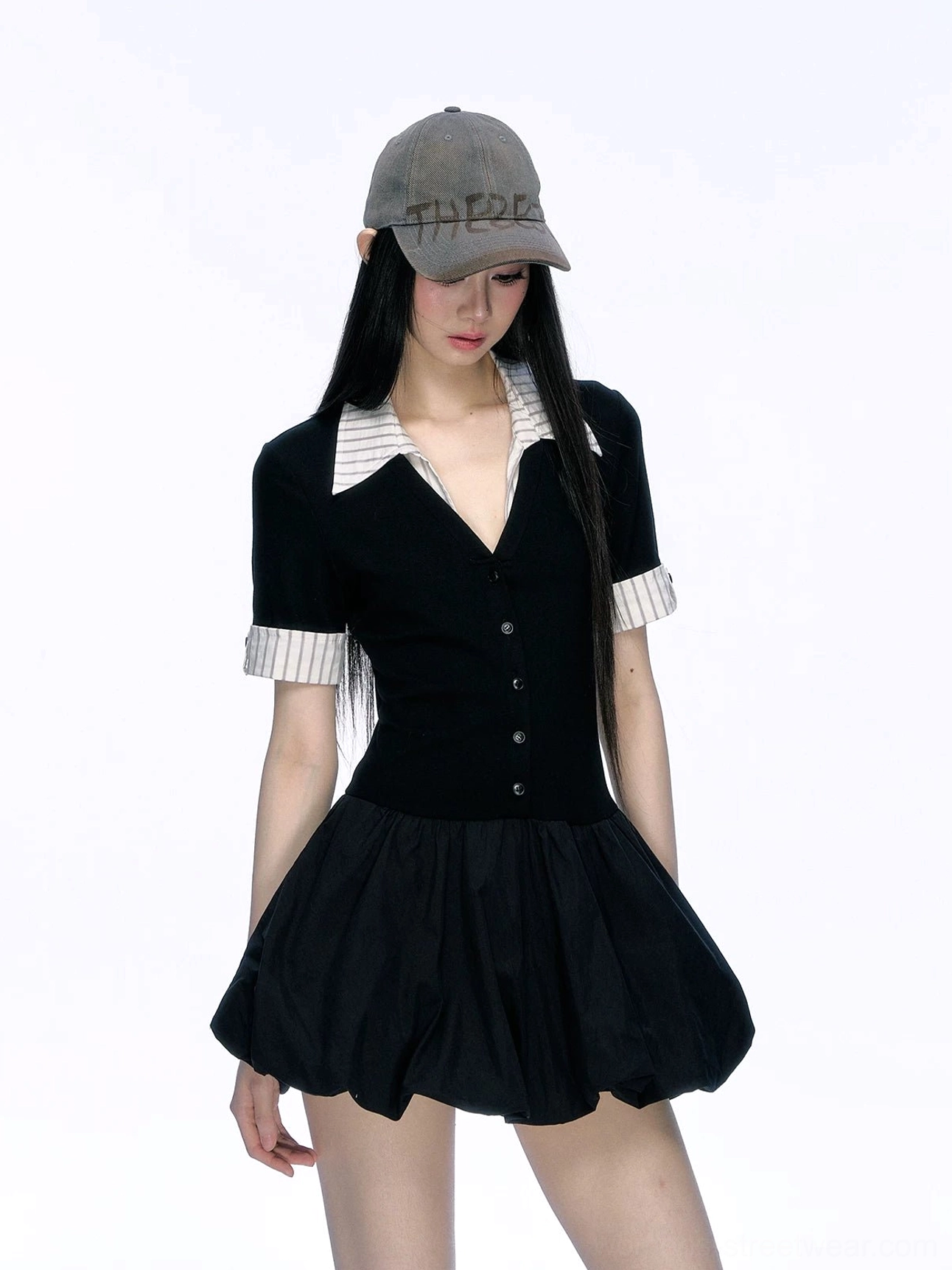 Front half-body view of black button-front contrast collar bubble hem mini dress styled with a gray baseball cap