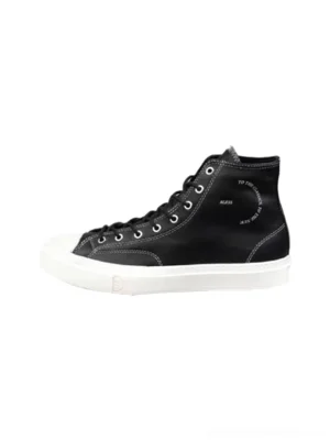 Black contrast-stitch platform high-top sneakers shown from a front three-quarter angle with white rubber toe caps, thick soles, metallic lace eyelets, and printed heel details