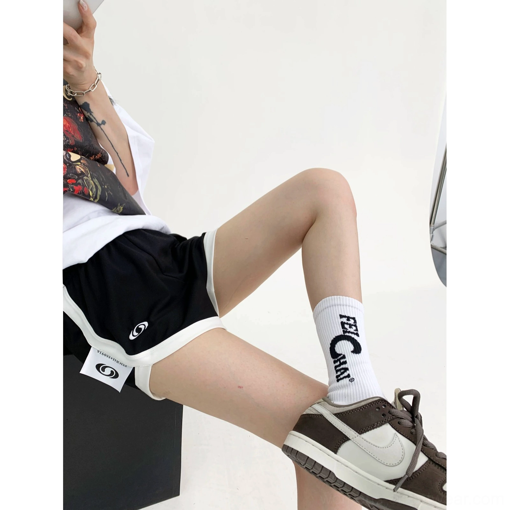 Side sitting view of black contrast trim athletic shorts styled with sneakers and socks for a casual Seoul streetwear outfit