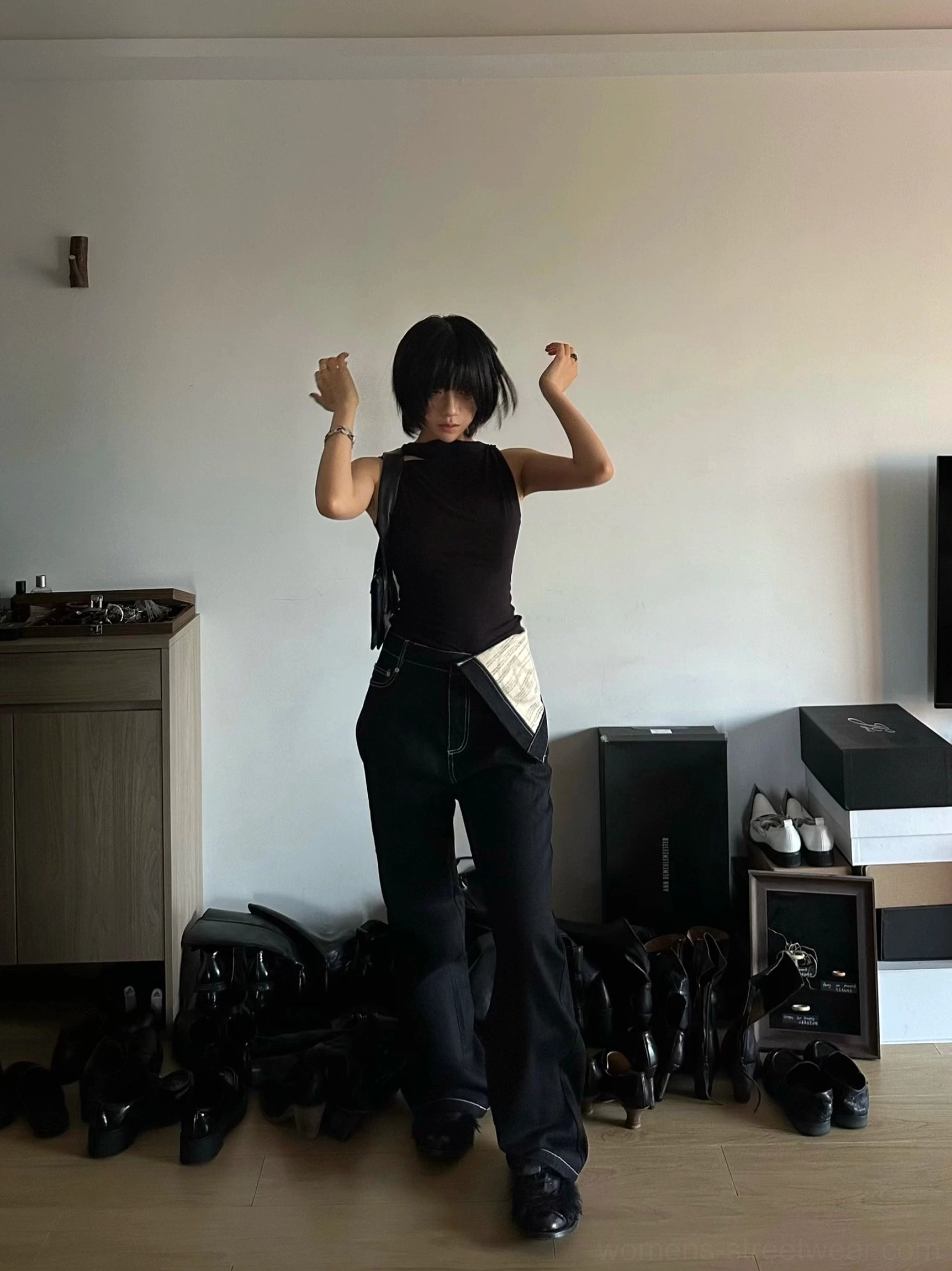 Female model styling black contrast waistband streetwear jeans with a fitted black sleeveless top in an indoor studio
