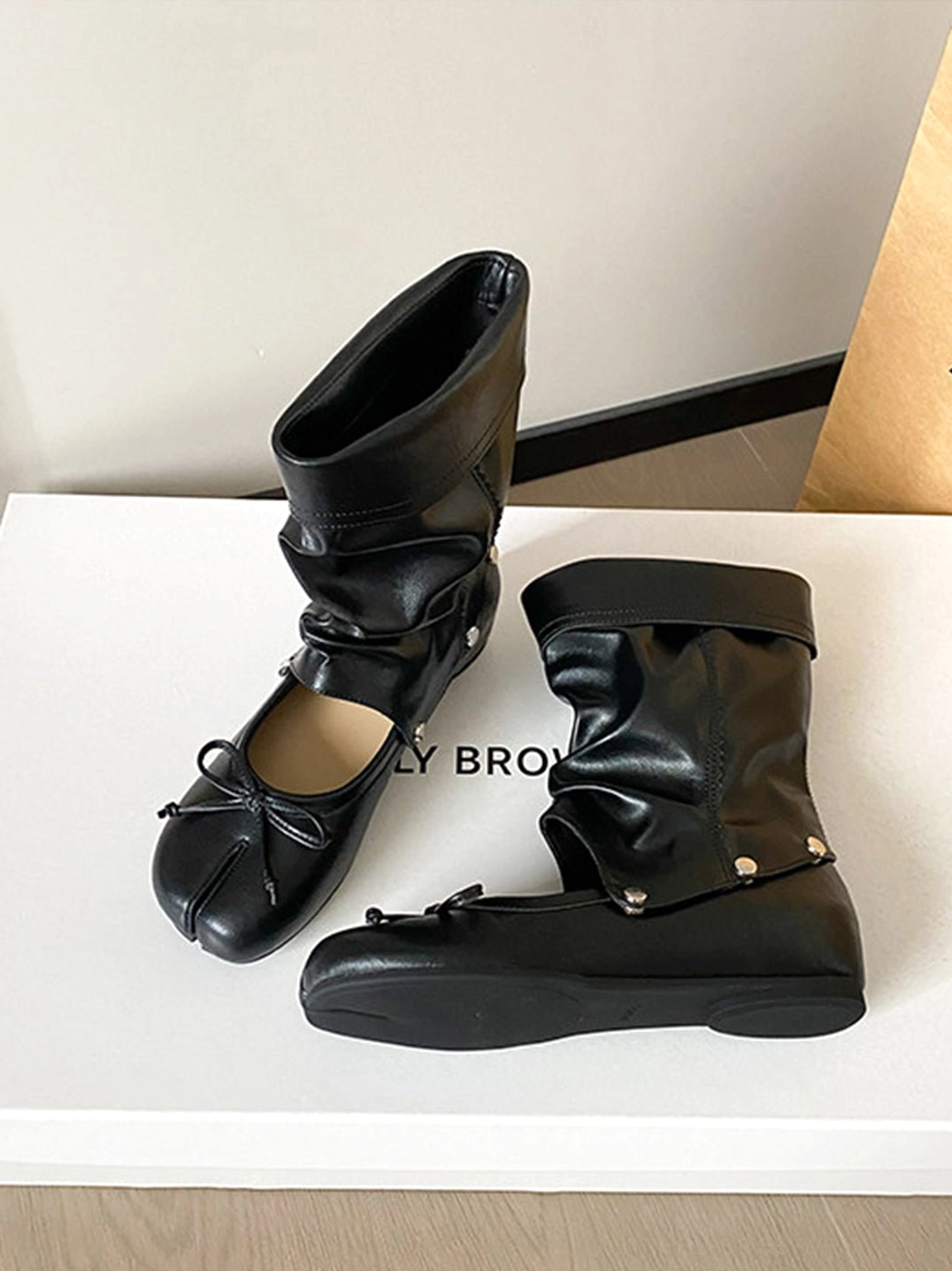 Black convertible tabi ballet sandal boots flat lay showing split-toe bow design and detachable studded shafts