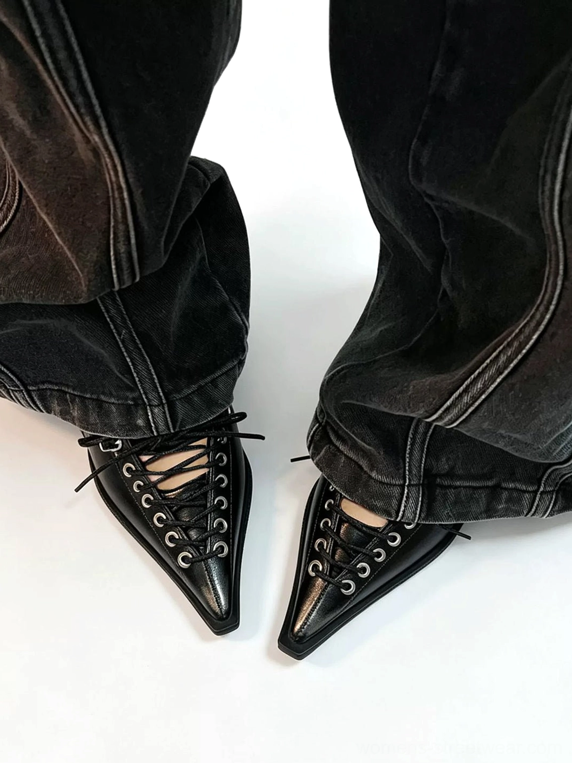 Black corset-lace pointed heel pump styling reference with sharp pointed toe, full metal eyelet lacing, and dark denim outfit