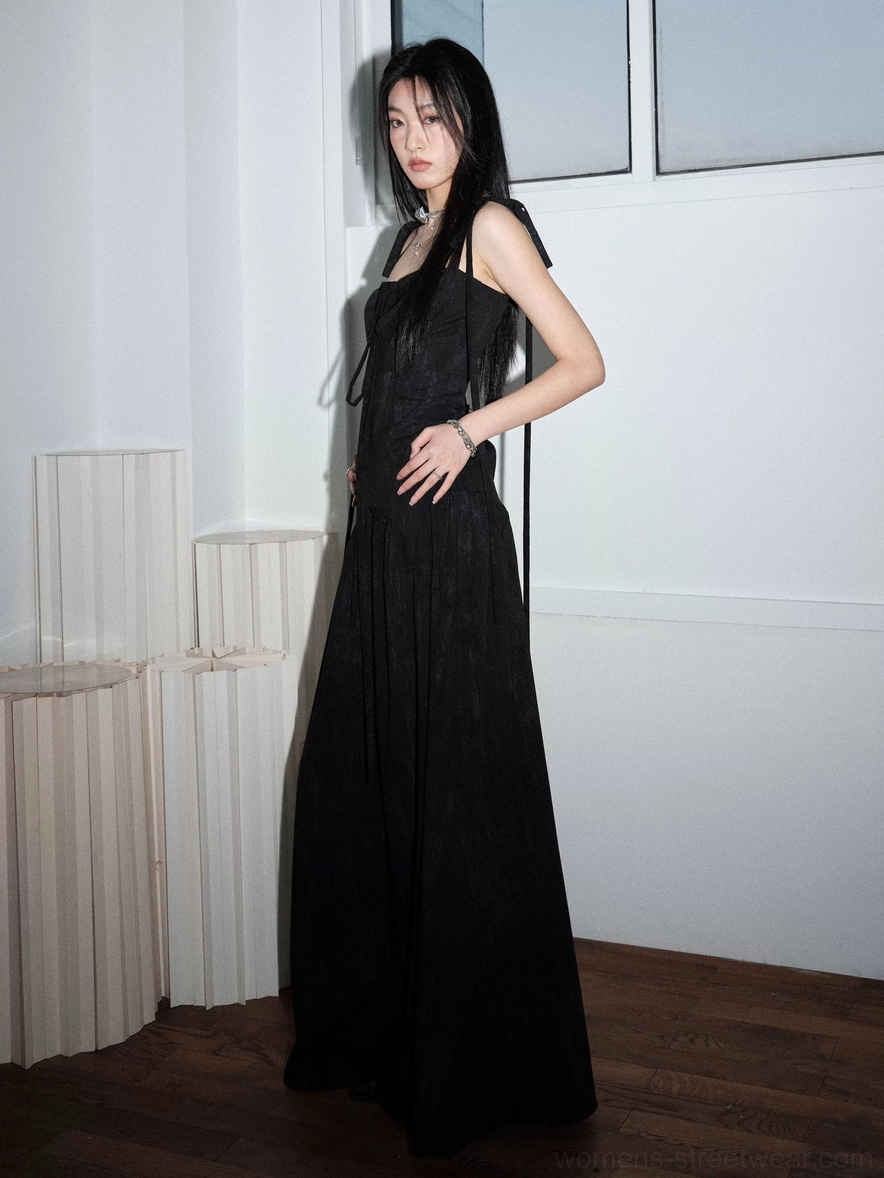 Side view of a black corset maxi dress with adjustable ribbon shoulder straps, slim bodice, defined waist, and long A-line skirt