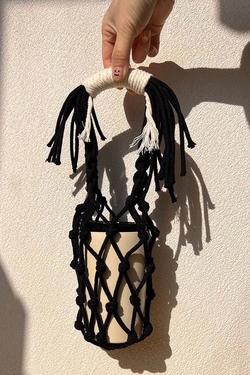 Black cotton macrame water bottle carrier with decorative tassel handle and flexible woven net pocket for everyday use