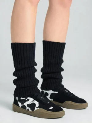 Black cow print low-top sneakers styled on female legs with black ribbed leg warmers in rear three-quarter view
