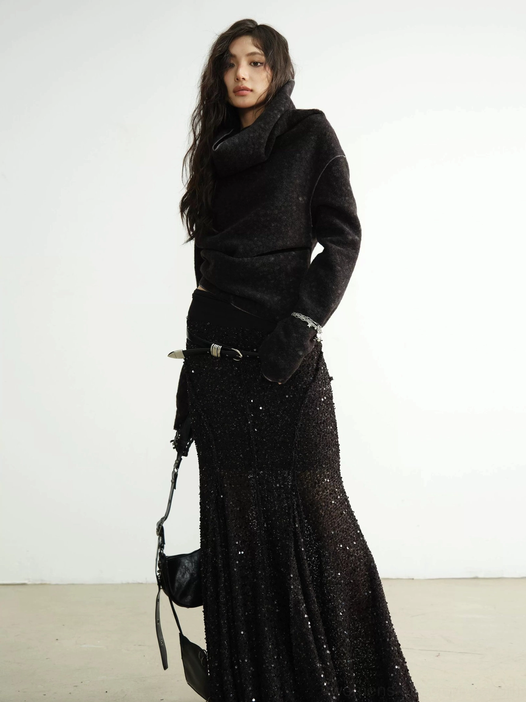 Black cowl-neck cropped textured knit cardigan paired with a fitted mermaid maxi skirt, metal waist belt, and black shoulder bag