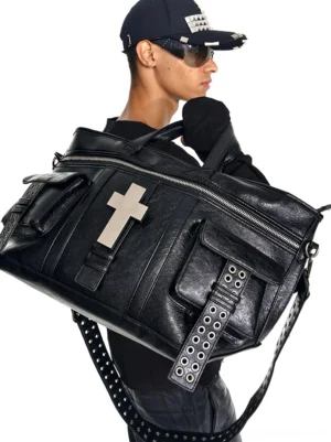 Streetwear model wearing black distressed leather crossbody tote bag with silver cross ornament and adjustable eyelet-studded shoulder strap