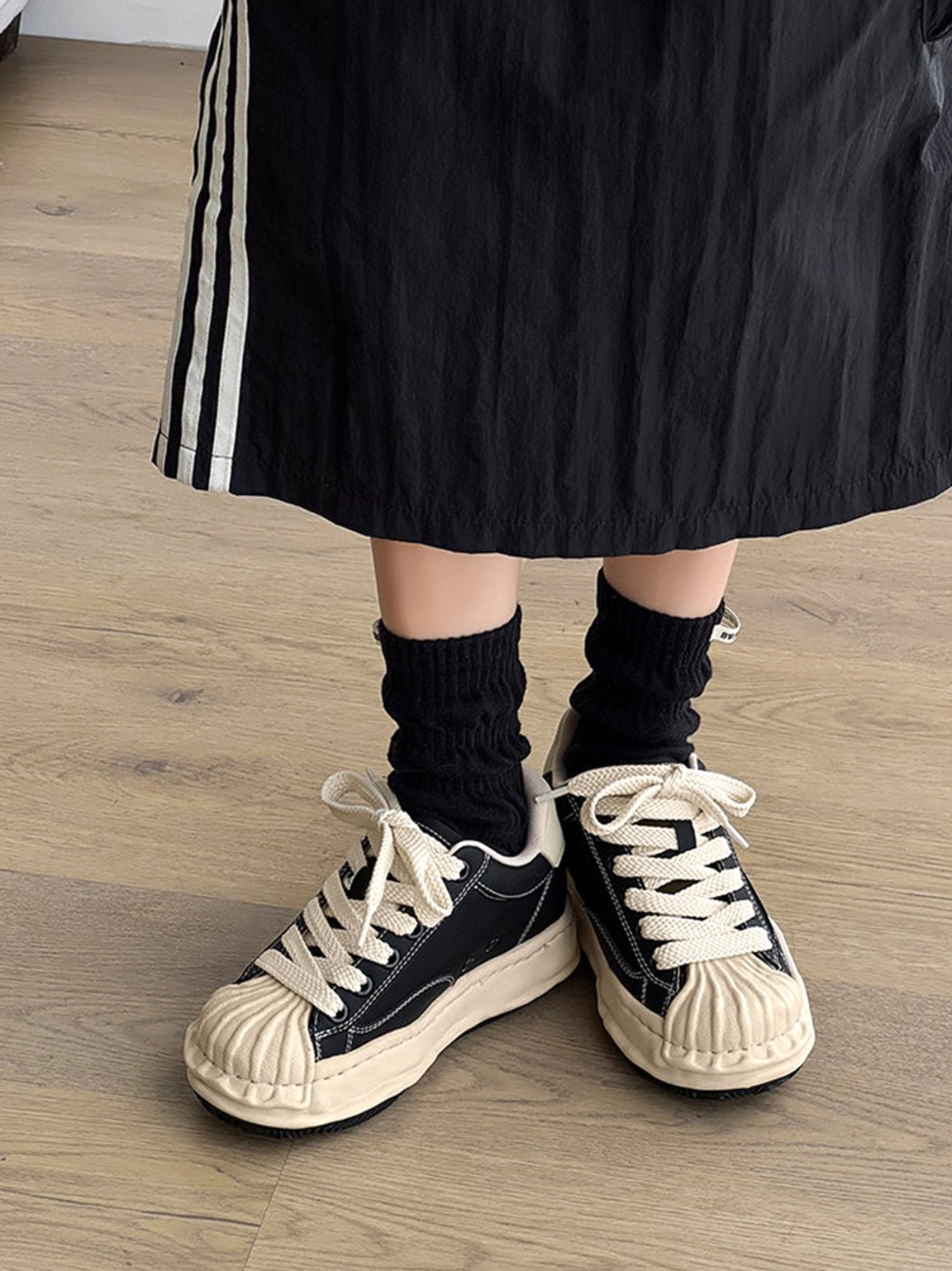 Front close-up of black and cream distressed platform sneakers with rounded shell toe and thick aged-style outsole