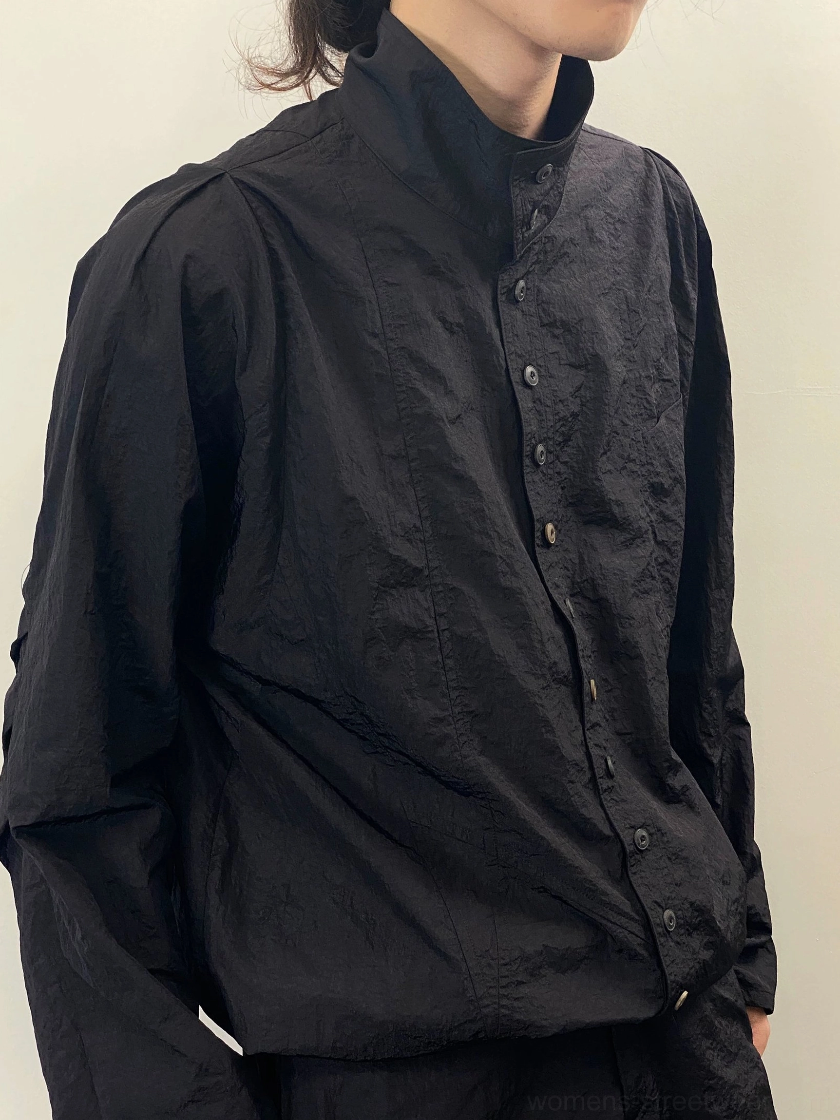 Close-up of black crinkled stand collar long sleeve shirt showing front buttons and dropped shoulder construction
