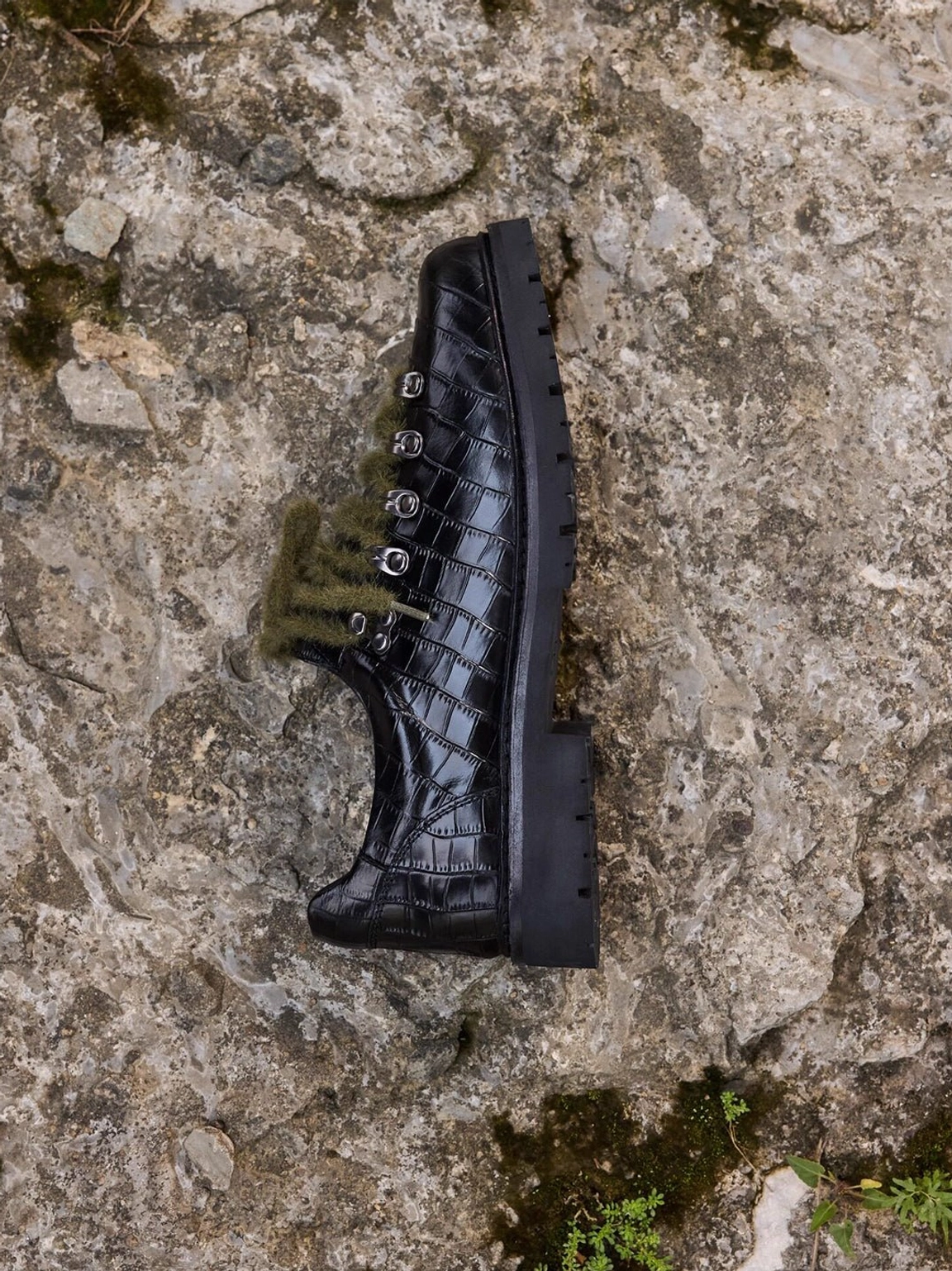 Side profile of a black croc-embossed leather derby shoe showing olive laces, metal eyelets, and thick rugged lug heel