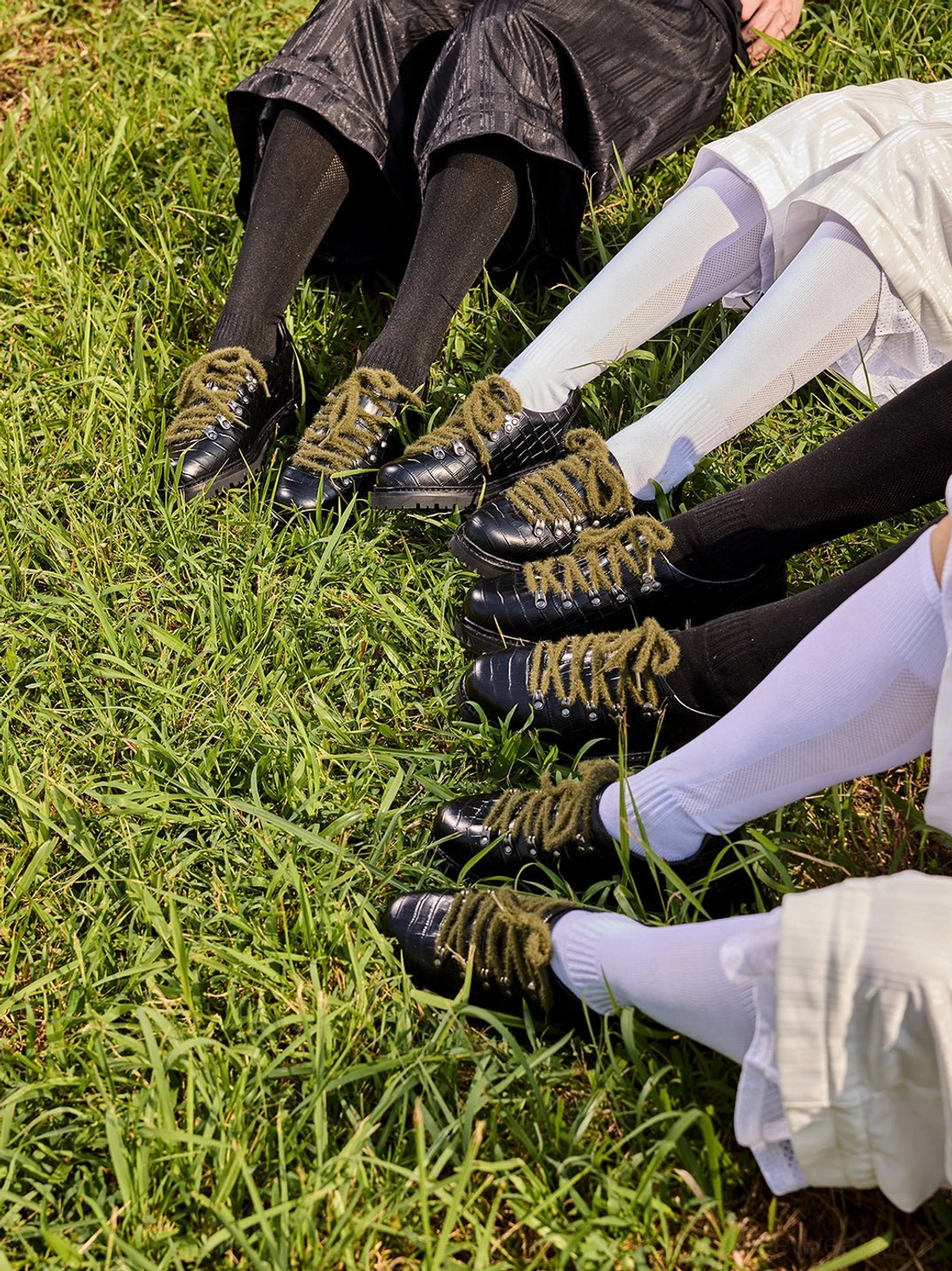 Multiple pairs of black croc-embossed derby shoes with olive laces displayed in a coordinated group fashion scene