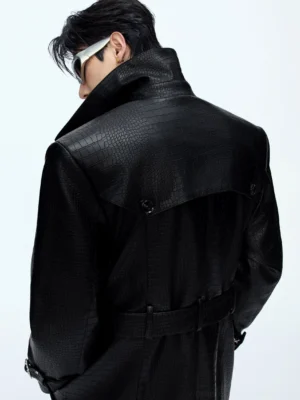 Back side close-up of black crocodile-textured leather trench coat showing glossy embossed grain back yoke waist belt and wide lapel