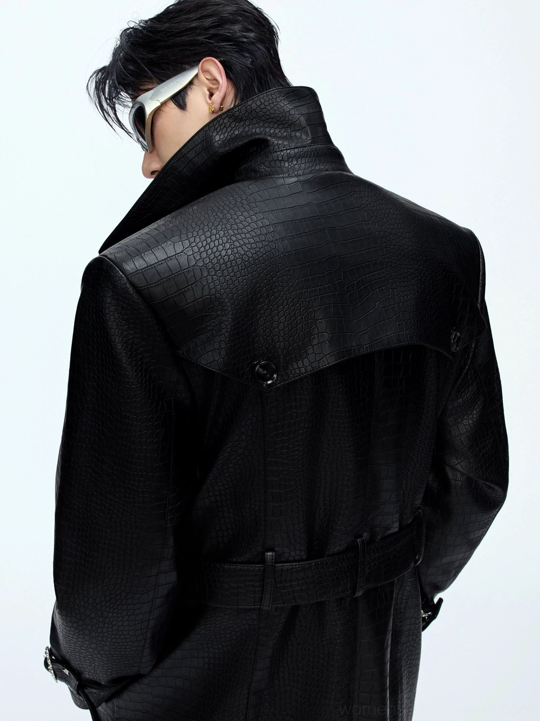 Back side close-up of black crocodile-textured leather trench coat showing glossy embossed grain back yoke waist belt and wide lapel