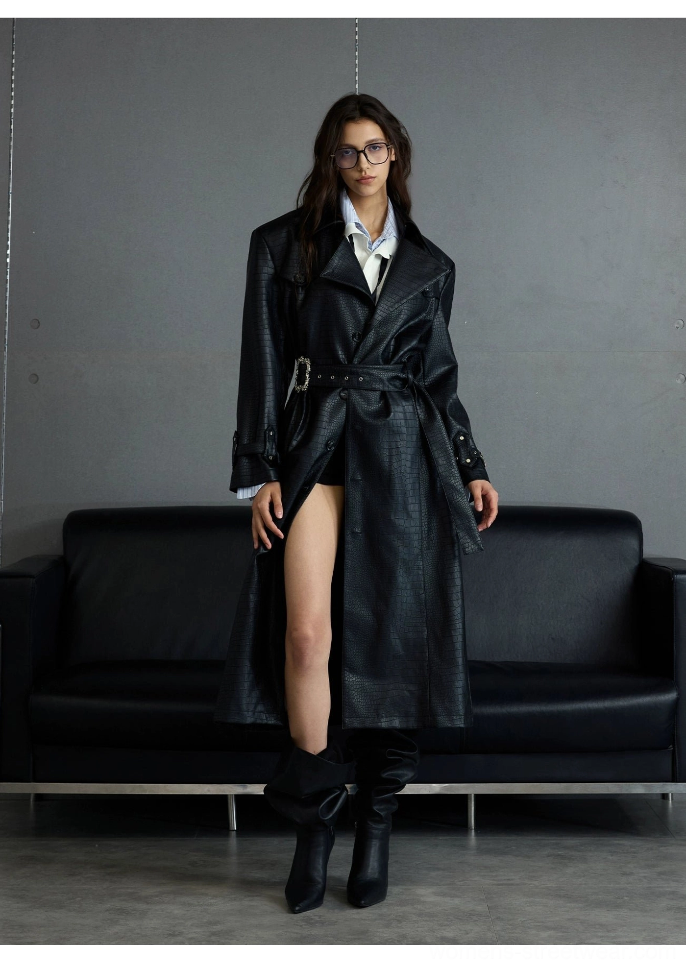 Front full-body womens styling of black croc-embossed leather trench coat with waist belt front slit white shirt and tall black boots