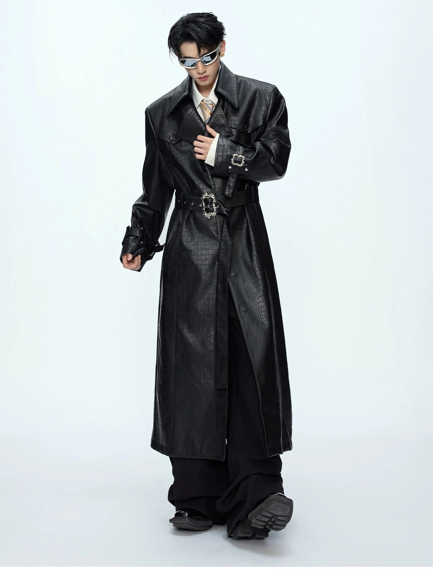 Three-quarter front view of black crocodile-textured leather trench coat featuring metallic belt buckle adjustable cuffs and notched lapels