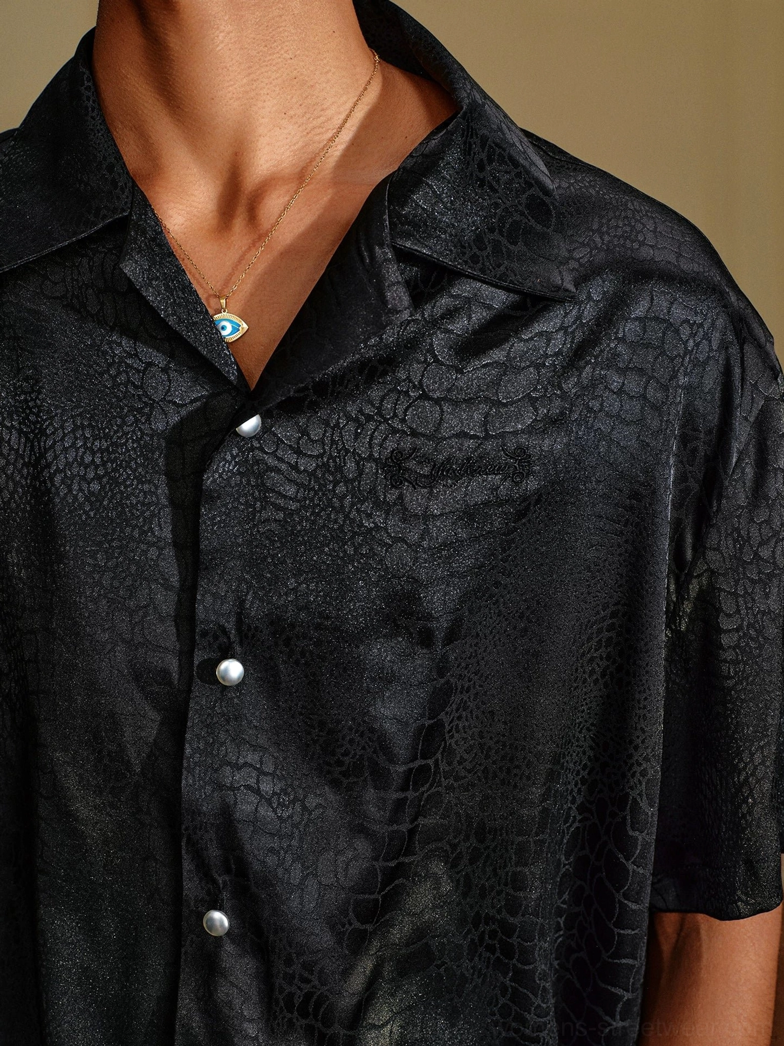 Close-up detail of black crocodile jacquard satin shirt collar, pearl-style buttons, embossed texture, and glossy front placket