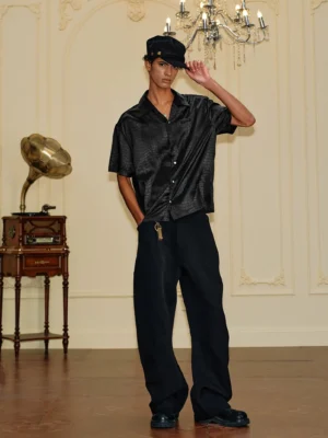 Side front view of a black crocodile textured satin shirt styled with wide-leg trousers in a vintage-inspired streetwear outfit