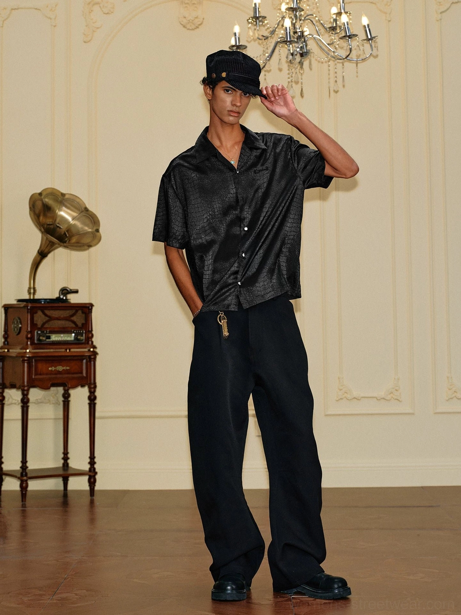 Side front view of a black crocodile textured satin shirt styled with wide-leg trousers in a vintage-inspired streetwear outfit
