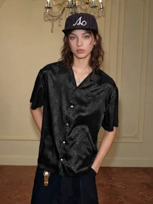 Front full-body view of a black crocodile jacquard satin short sleeve streetwear shirt with relaxed fit, open camp collar, and glossy textured fabric