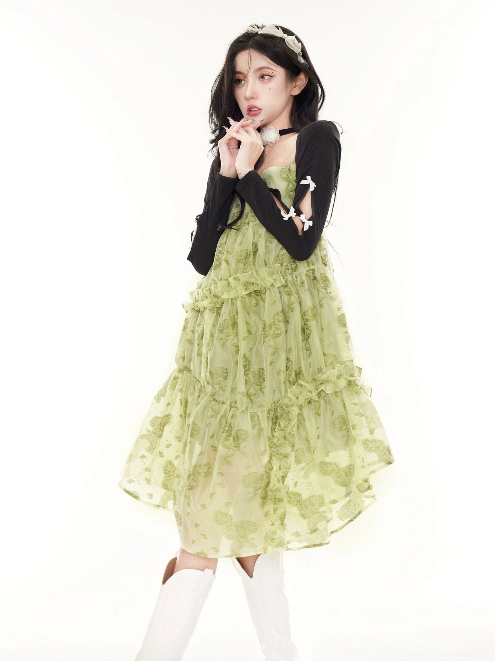 Black cropped sun cardigan layered over a green floral ruffle slip dress with bow sleeve details and white boots