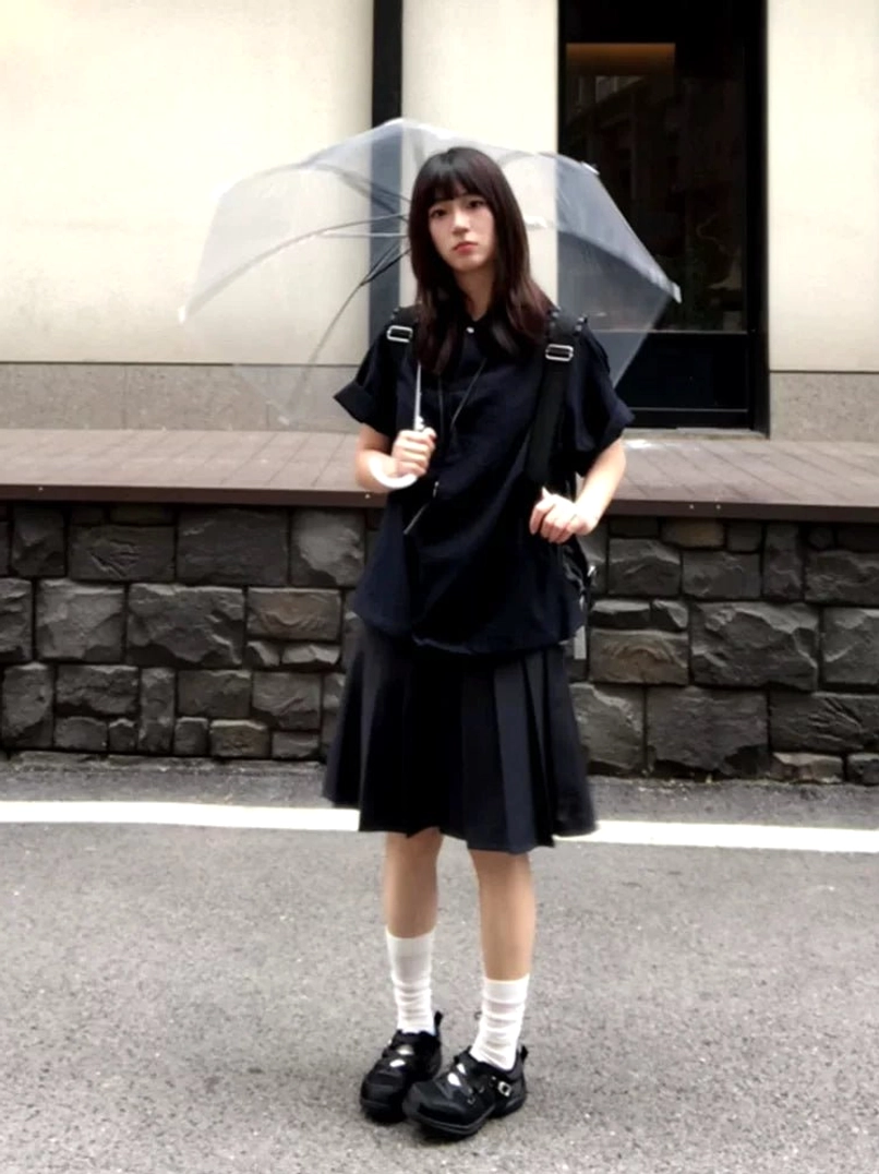 Young woman wearing black cross-strap cutout sneakers with white crew socks and an all-black Y2K streetwear outfit on an urban sidewalk