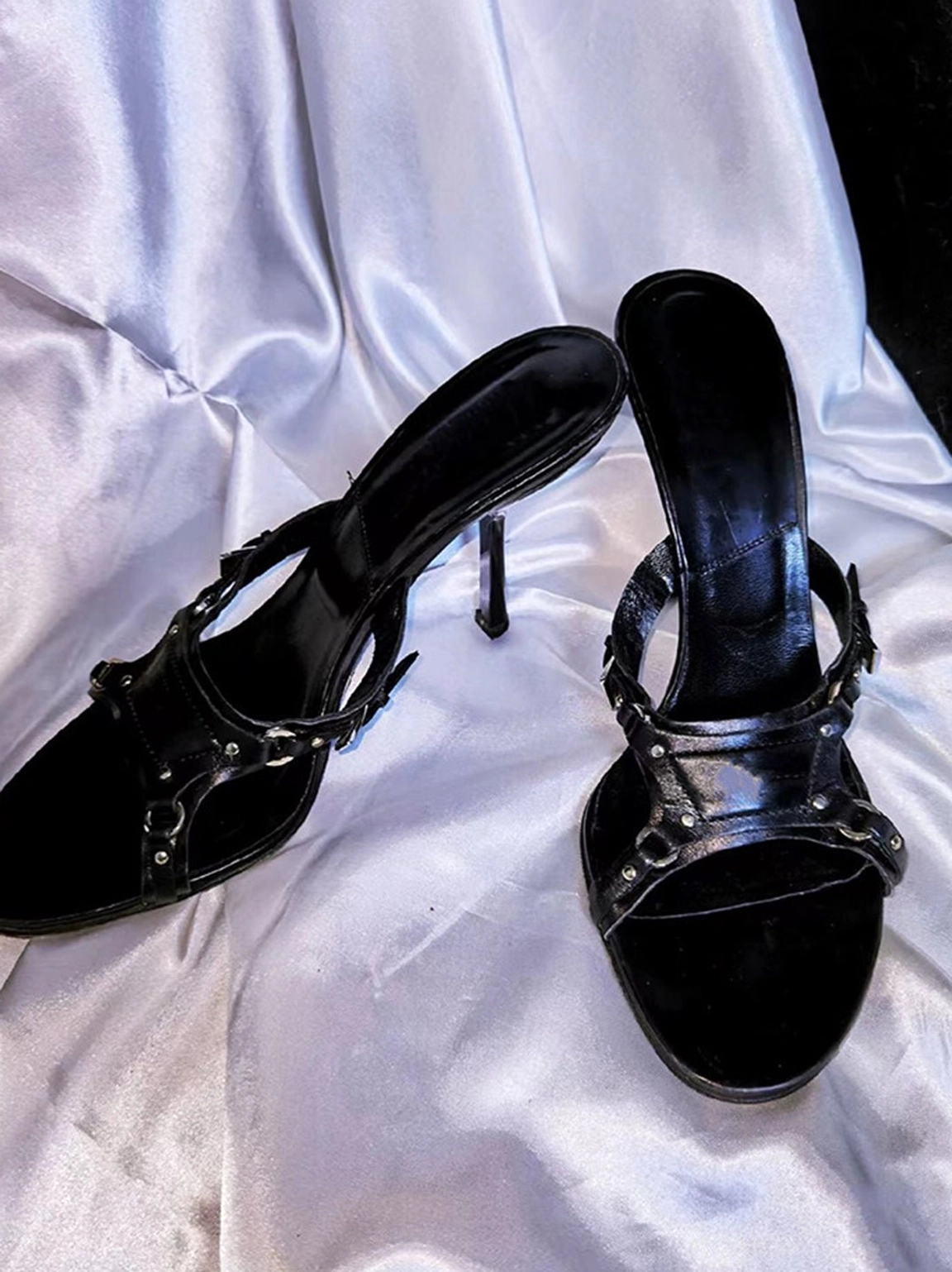 Black cross-strap open-toe stiletto sandals displayed from front and side angles with metallic ring and rivet embellishments