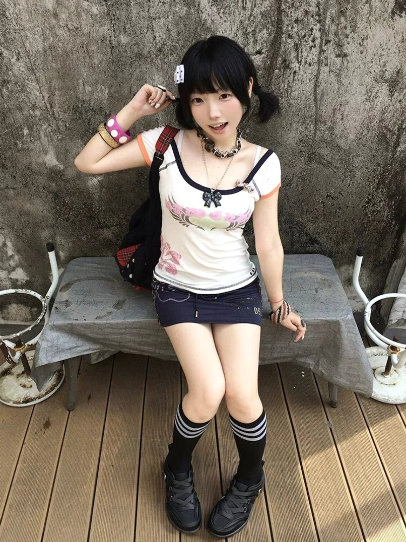 Y2K streetwear styling with black cross-strap sneakers, striped knee-high socks, and a casual layered outfit in an urban terrace setting