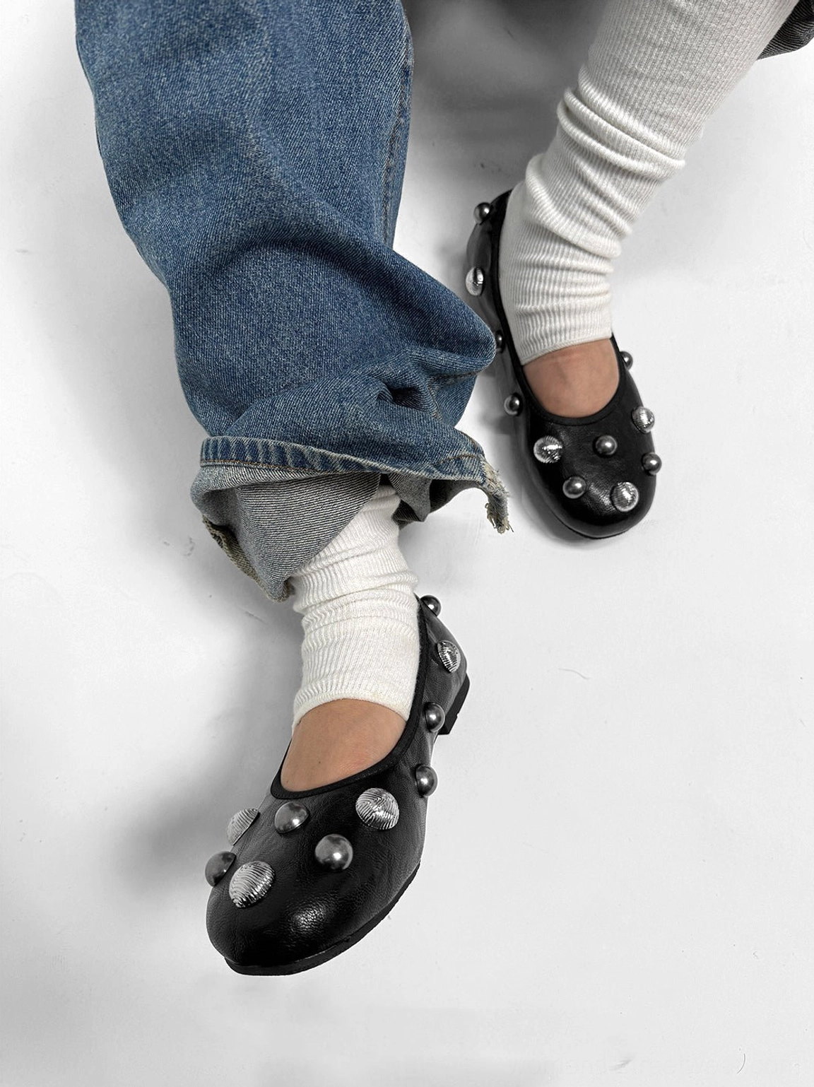 Side three-quarter view of a black crystal stud ballet flat worn with white socks and rolled blue jeans