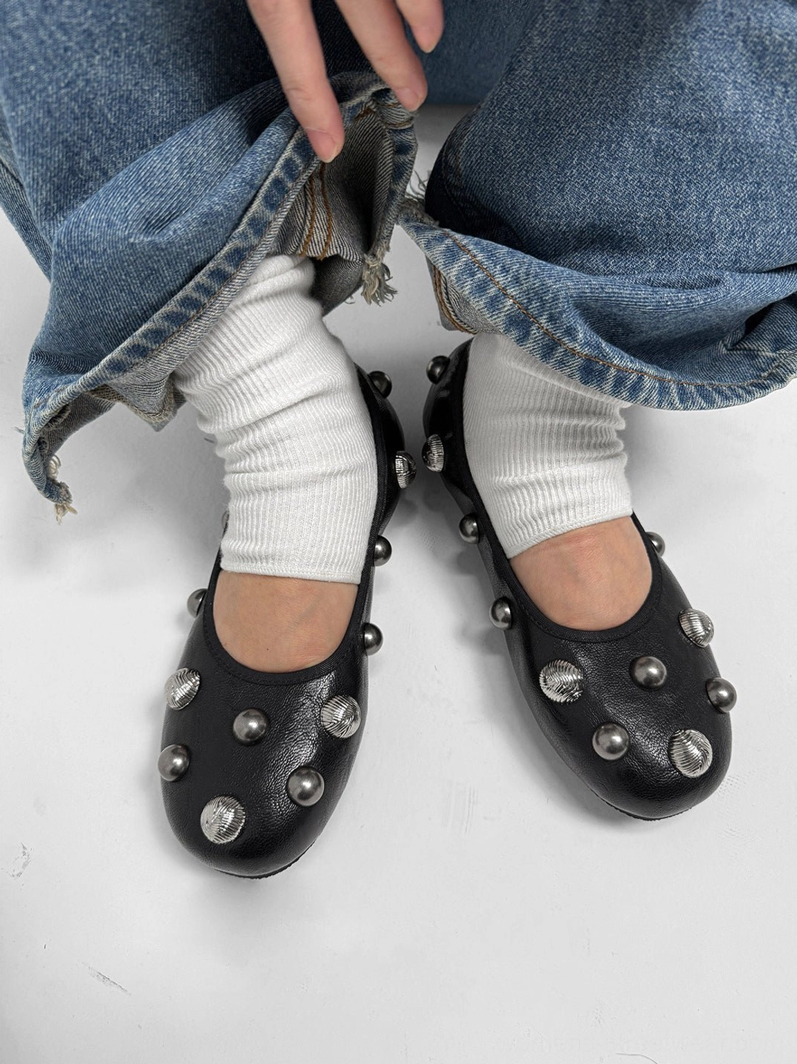 Pair of black studded ballet flats worn with white socks and frayed rolled hem blue jeans, viewed from above