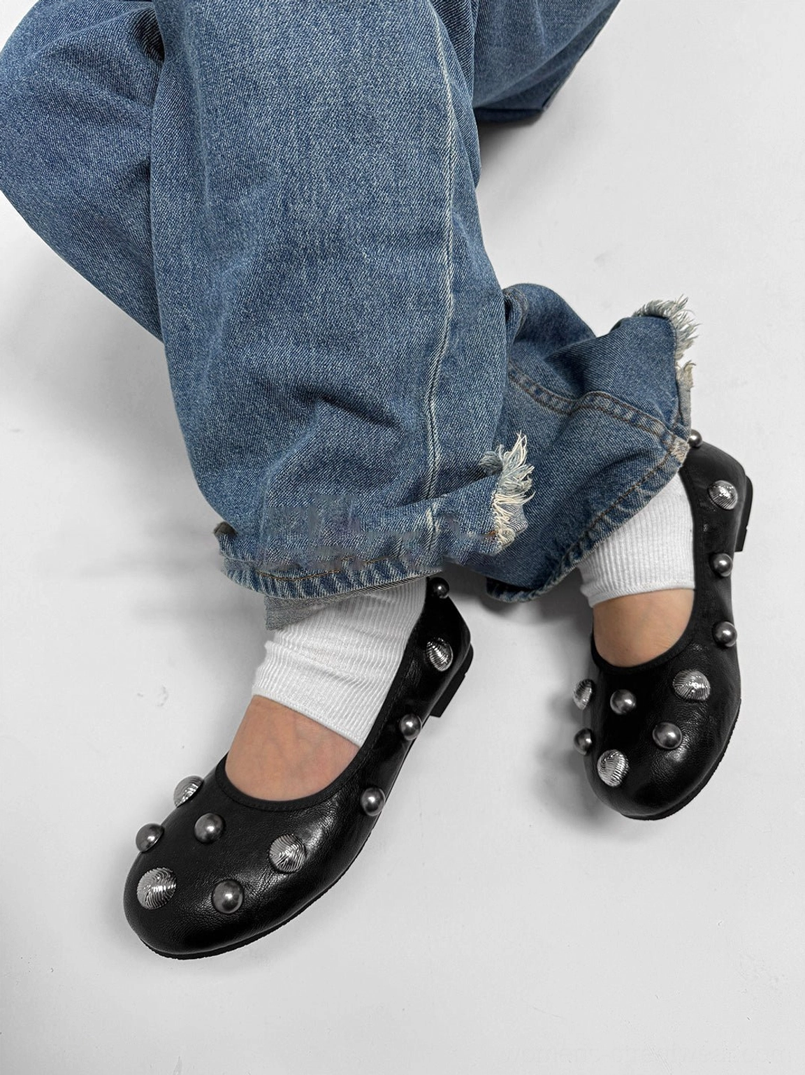 Black studded ballet flats paired with rolled hem blue denim and white socks, showing the decorated toe and flat sole edge