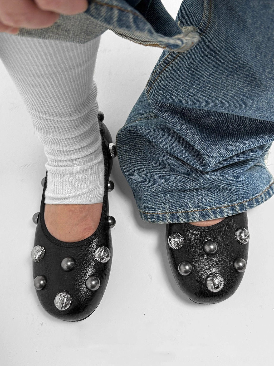 Top-down view of black crystal stud ballet flats styled with white slouch socks and blue jeans, highlighting silver toe studs