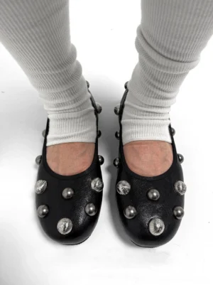 Black studded ballet flats worn with white ribbed socks, showing silver crystal studs across the vamp and rounded toe