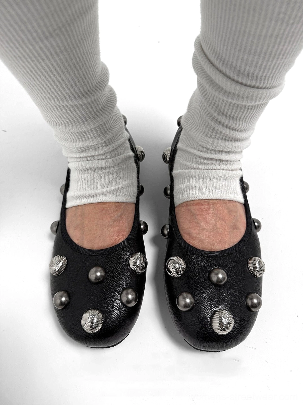 Black studded ballet flats worn with white ribbed socks, showing silver crystal studs across the vamp and rounded toe