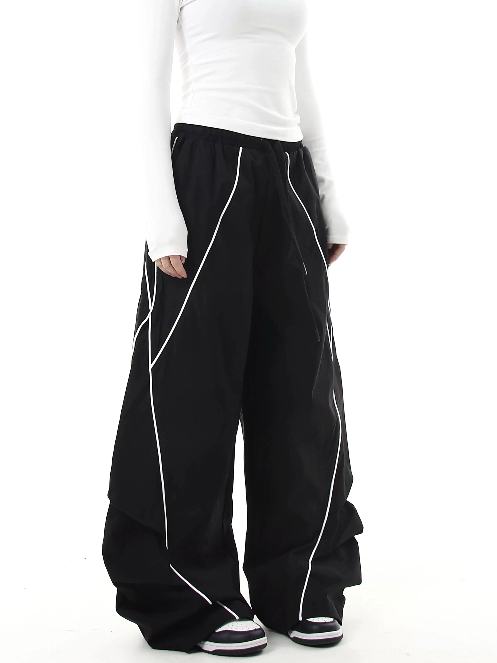 Side view of black curve-leg cargo pants featuring diagonal reflective linework, sculpted draped seams, wide-leg construction, and futuristic techwear styling