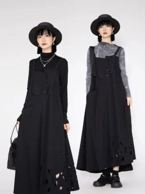 Front three quarter view of a black cutout hem pinafore maxi dress with slim straps, front buttons, patch pockets, and relaxed Korean streetwear layering