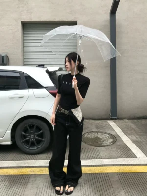 Female model wearing black deconstructed contrast waist straight-leg jeans with relaxed full-length fit outdoors beside a white car