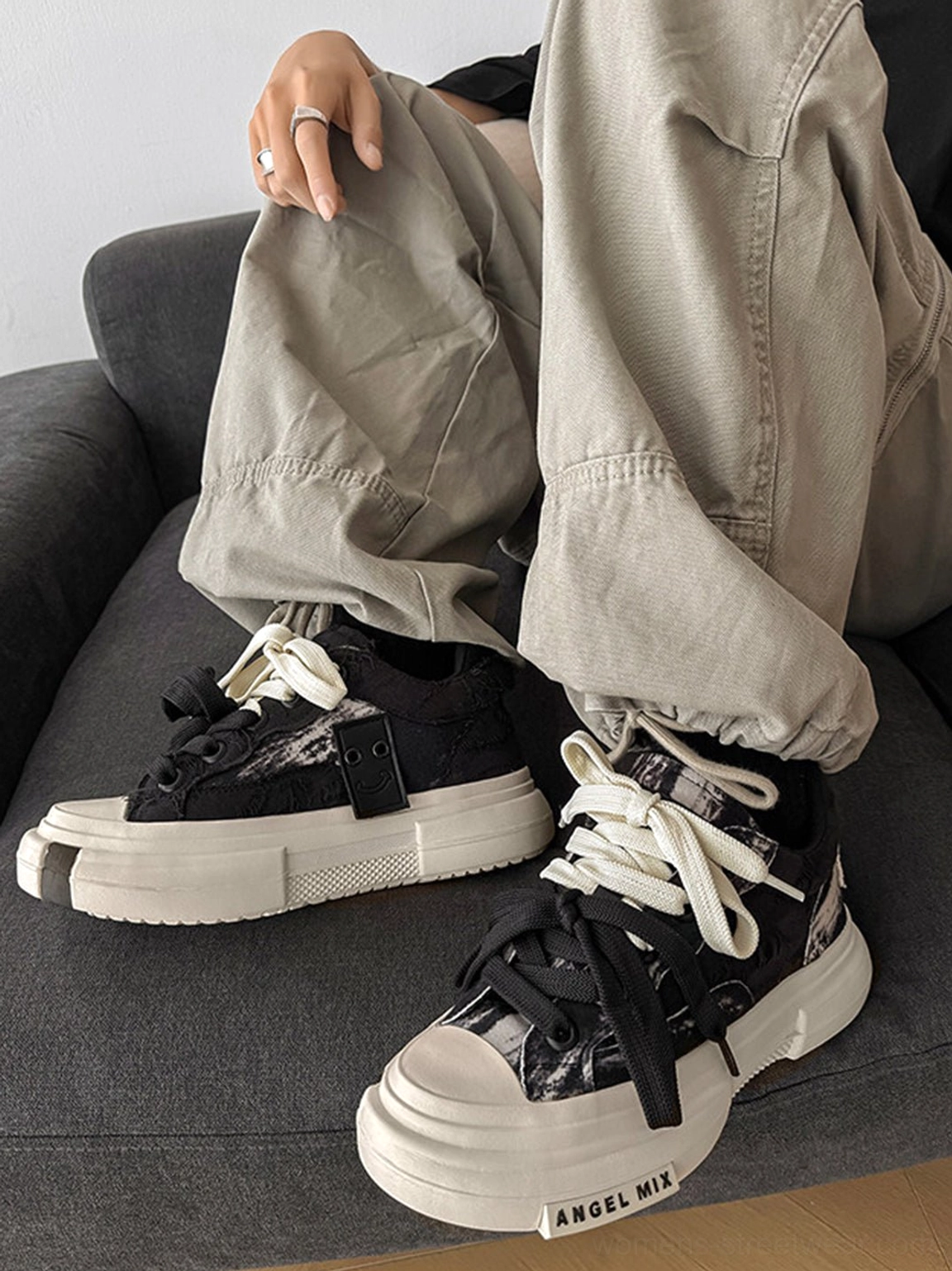 Side view of black and white distressed canvas platform sneakers worn with loose gray cargo pants showing the thick sole and front construction