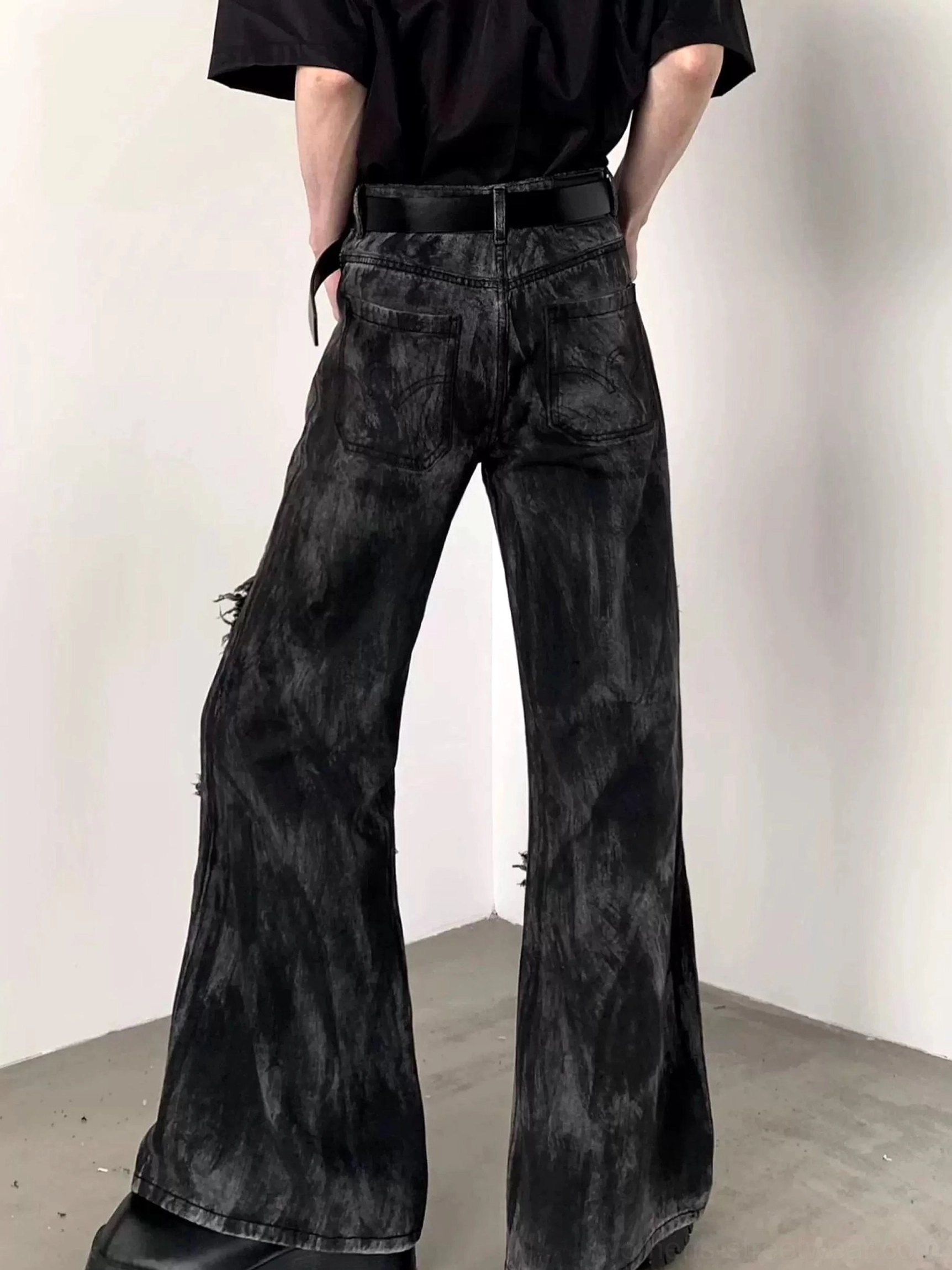 Back view of black distressed flared jeans showing the vintage washed finish, rear waistband, back pockets, frayed seams, and wide-leg shape