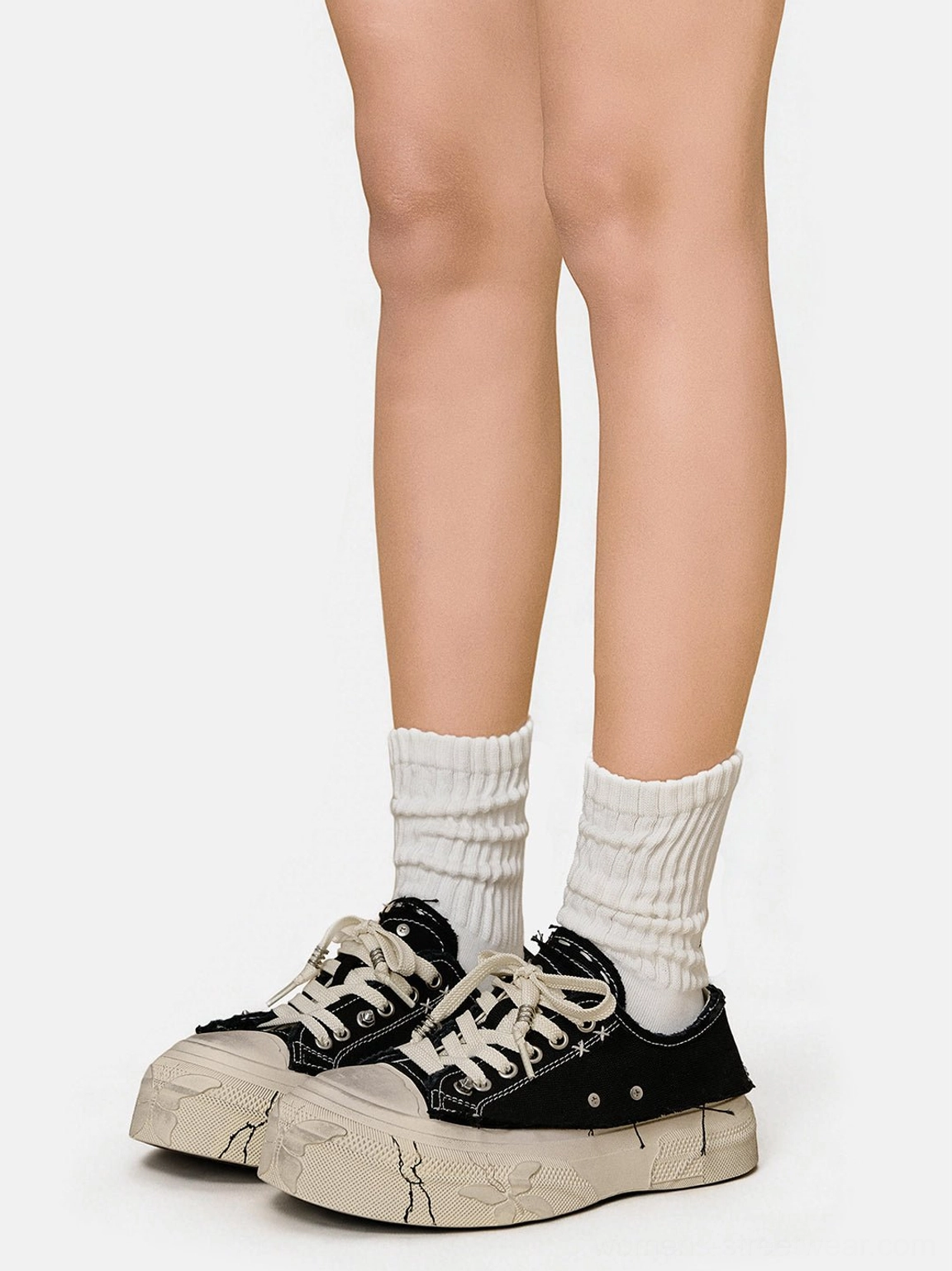 Front view of black distressed platform canvas sneakers with white mid-calf socks and cracked off-white platform soles