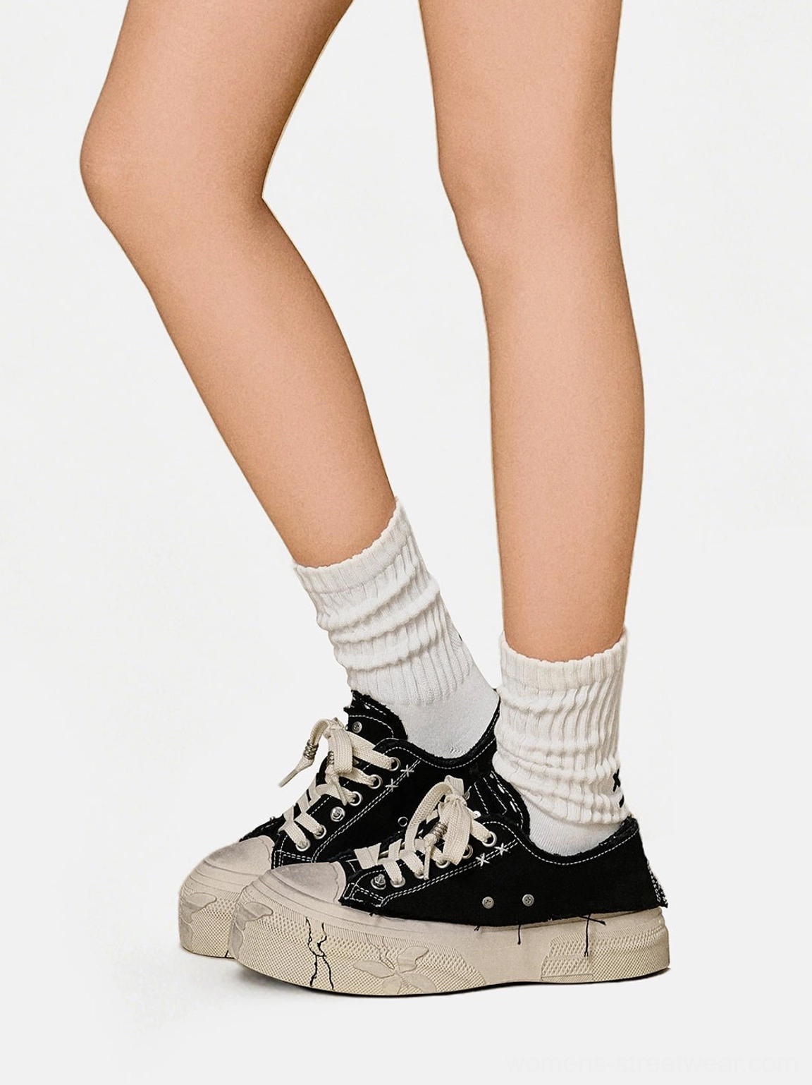 Black distressed platform canvas sneakers worn with white crew socks in a low-angle streetwear studio view