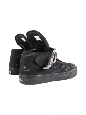 Side and rear three-quarter view of black high-top canvas sneakers featuring distressed fabric, all-black rubber outsoles, fold-over tongues, wing hardware, and spiked ankle straps