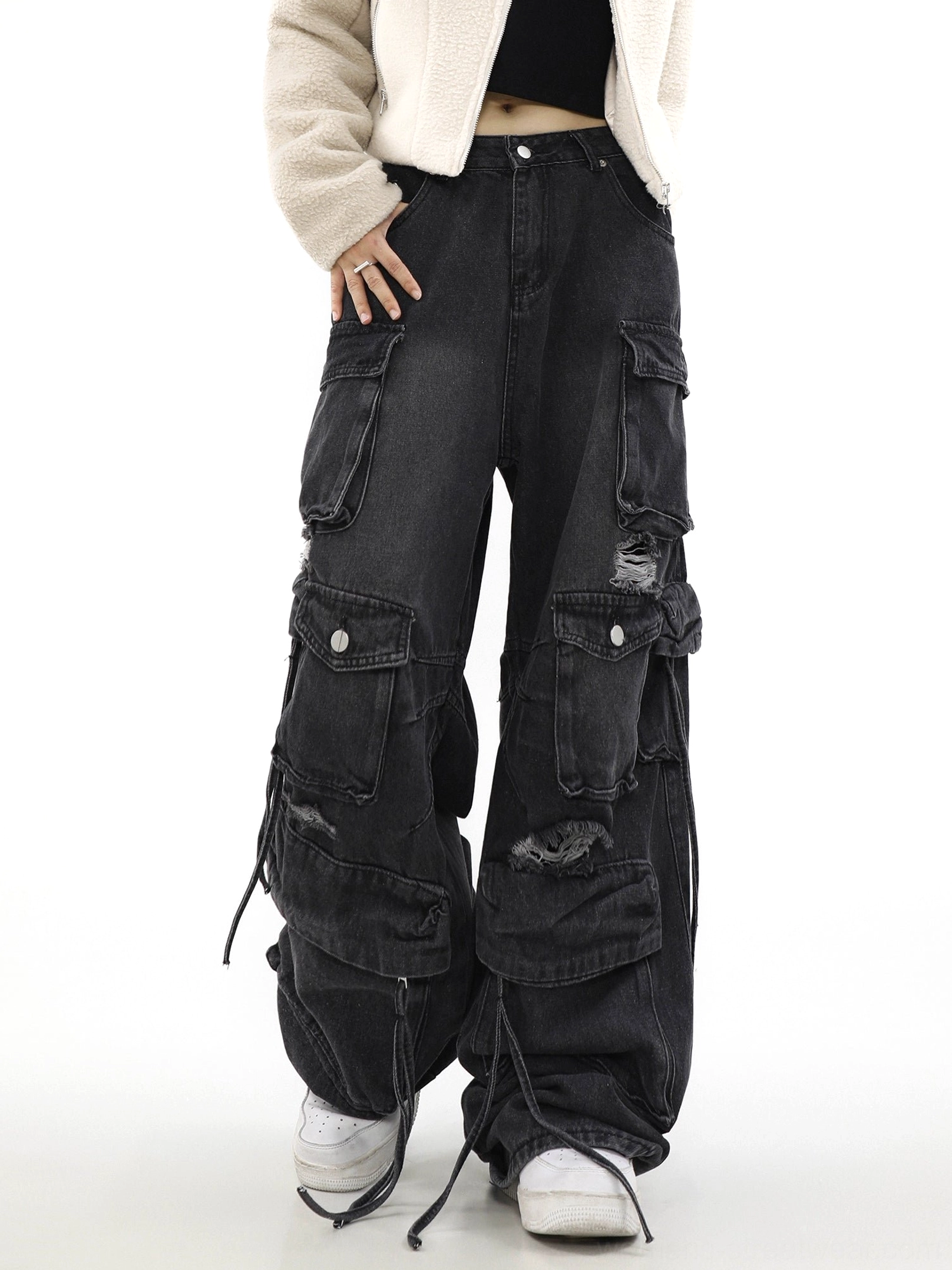 Three-quarter model view of black distressed utility cargo jeans with asymmetric pockets, baggy legs, and adjustable drawstring hems