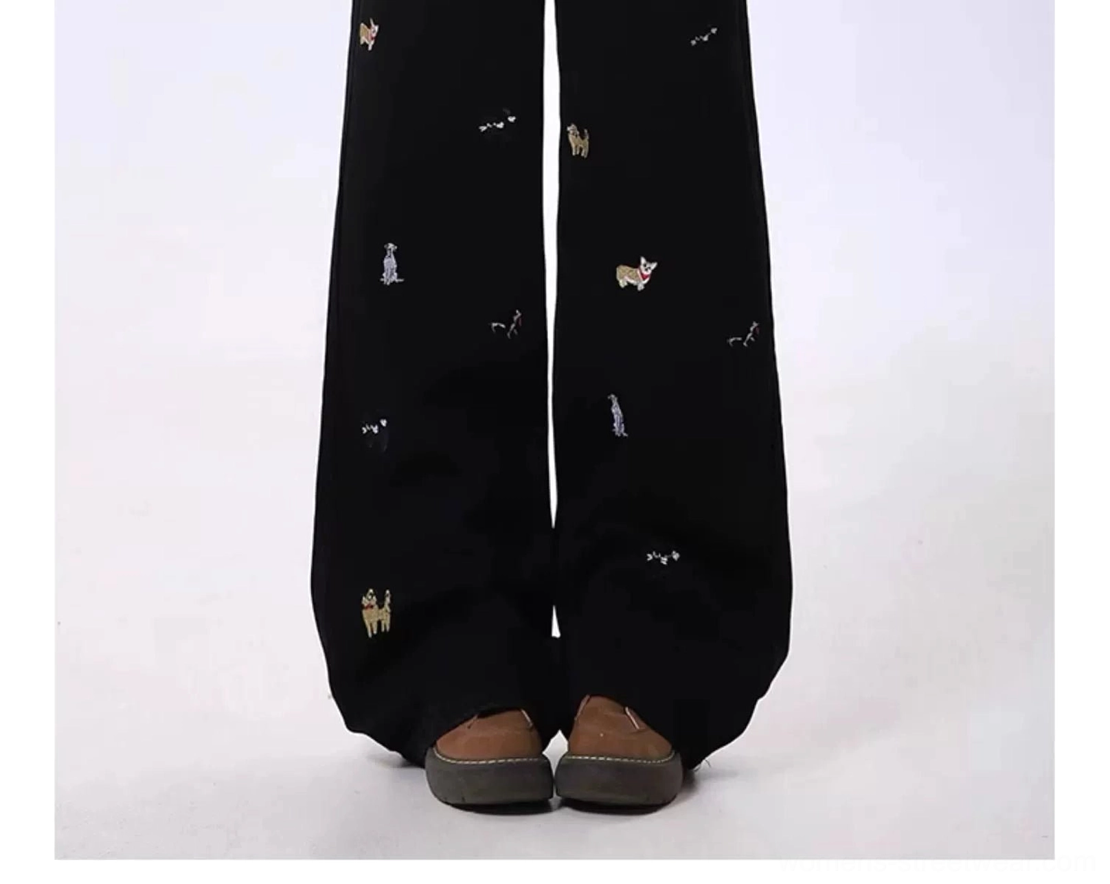 Close up of black wide leg denim jeans featuring delicate dog pattern embroidery on the lower legs