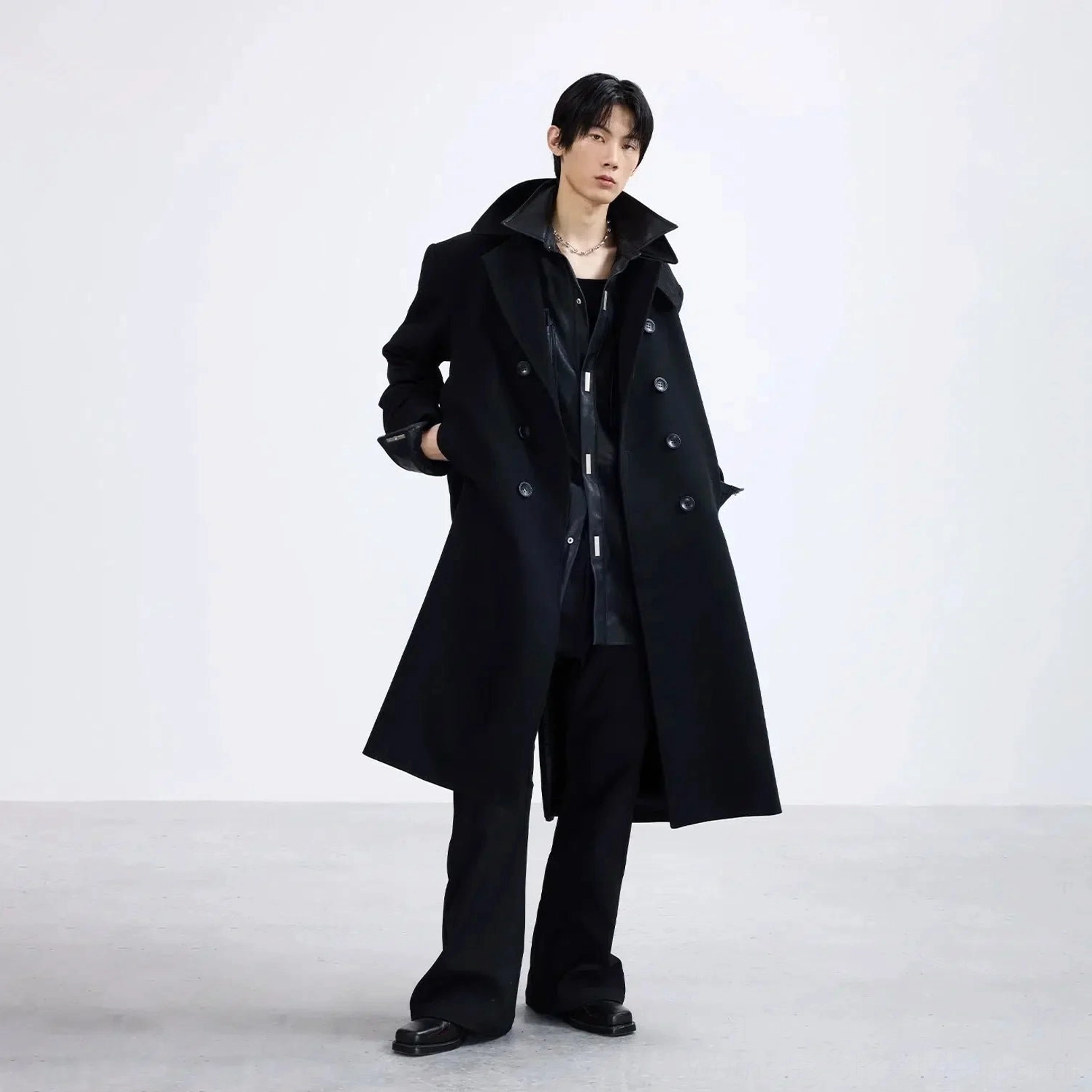 Three-quarter view of a relaxed oversized black double-breasted overcoat with notched lapel styled with shirt and tailored trousers