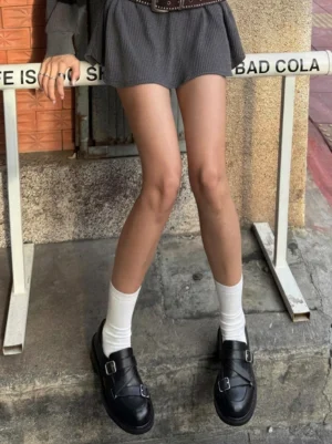 Female model wearing black double-buckle block-heel loafers with white crew socks and a gray mini skirt in a Seoul-inspired streetwear outfit