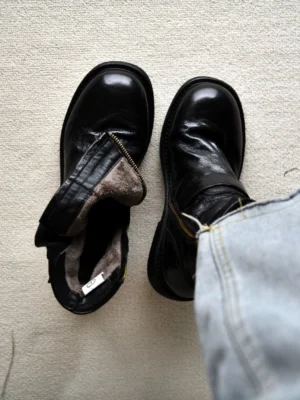 Black double buckle leather ankle boots flat lay with denim jeans showing side zipper closure warm faux fur lining and rubber sole