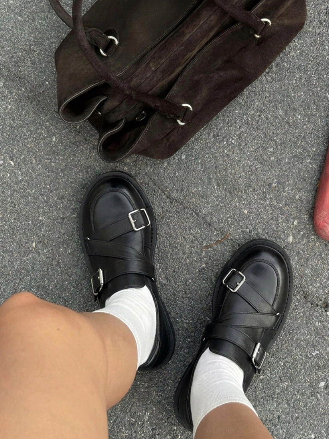 Top-down view of polished black double-buckle loafers worn with white socks beside a brown leather bag for urban street style
