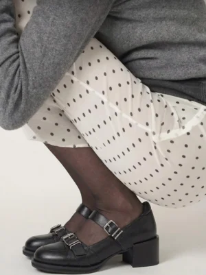 Black double-buckle Mary Jane shoes styled with polka-dot tights, sheer black socks, and a casual grey streetwear outfit