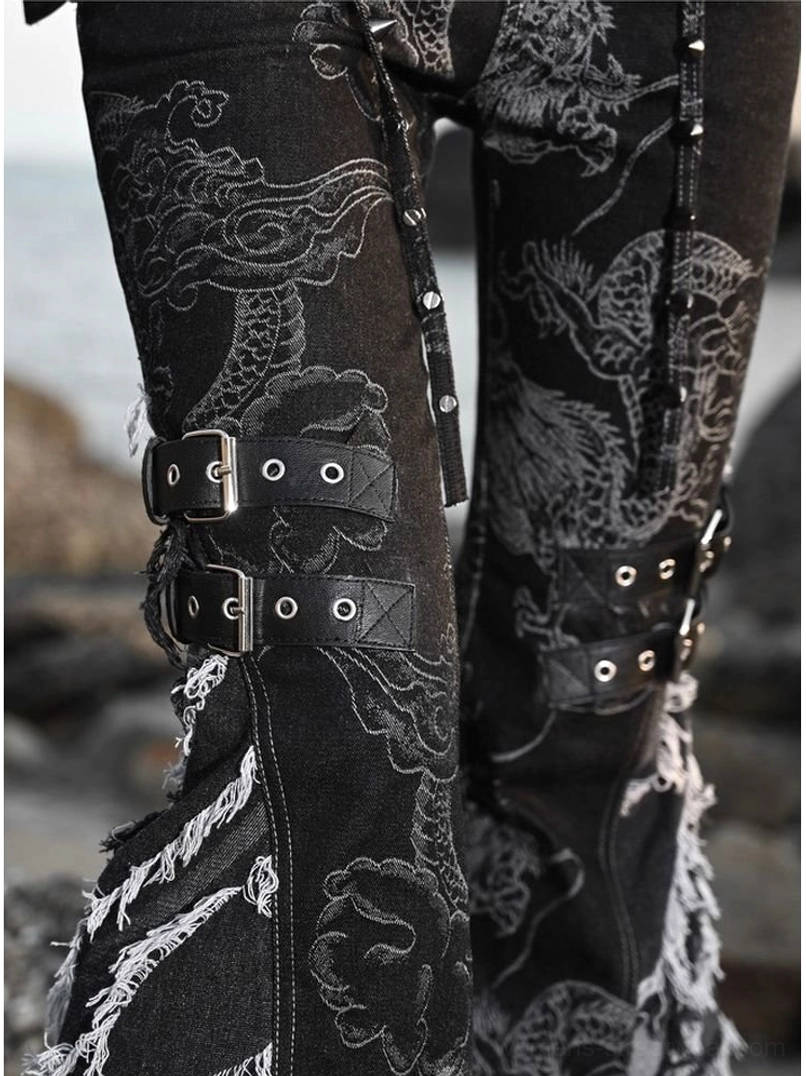 Side close up of black dragon print flare jean legs with knee buckle straps, metal stud fasteners, frayed denim edges, and gothic western details