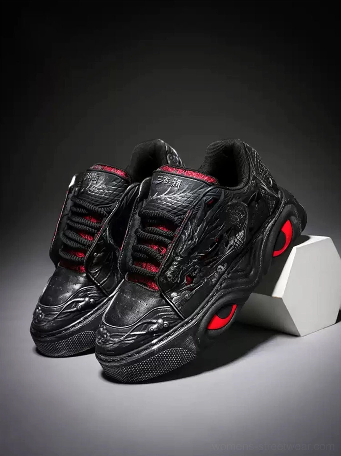 Pair of black dragon relief chunky platform sneakers shown from a front three-quarter angle with embossed uppers and curved red-accented soles